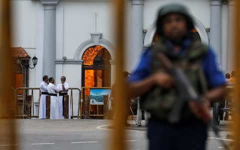 Priests are seen in the background as a security personnel stands guard in front of St Anthony's Shrine, struck by IS-linked terrorists on Easter Sunday - Credit: DANISH SIDDIQUI/&nbsp;REUTERS
