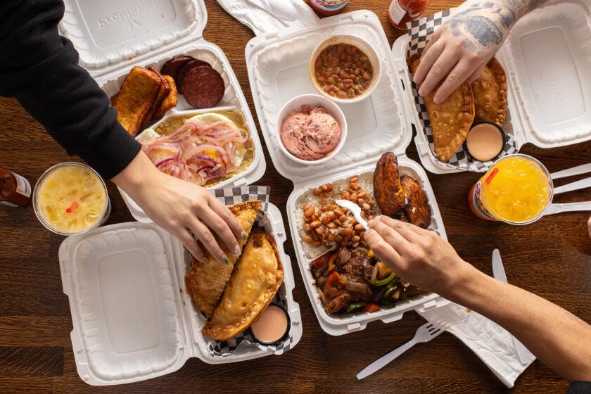 NORTH HOLLYWOOD, CA - MARCH 1: Guests hands shown dining on Mangu los tres golpes (mashed, boiled plantains, fried eggs, pickled red onion, fried salami and cheese) and Santana's Chicken (sauteed chicken, marinated in garlic, onion, oregano, cilantro and spices, served with white rice, beans, fried plantains and beet and potato salad), and empanadas on an interior dining table at El Bacano Restaurant on Friday, March 1, 2024 in North Hollywood, CA. (Catherine Dzilenski / For The Times)