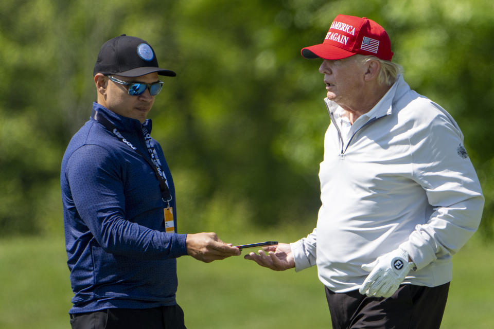 Walt Nauta, left, takes a phone from Former President Donald Trump during the LIV Golf Pro-Am at Trump National Golf Club, Thursday, May 25, 2023, in Sterling, Va. When Trump appears in federal court in Miami, he will likely be joined on the witness stand by a man well-practiced in standing by his side: auta, his valet turned co-conspirator. (AP Photo/Alex Brandon, File)