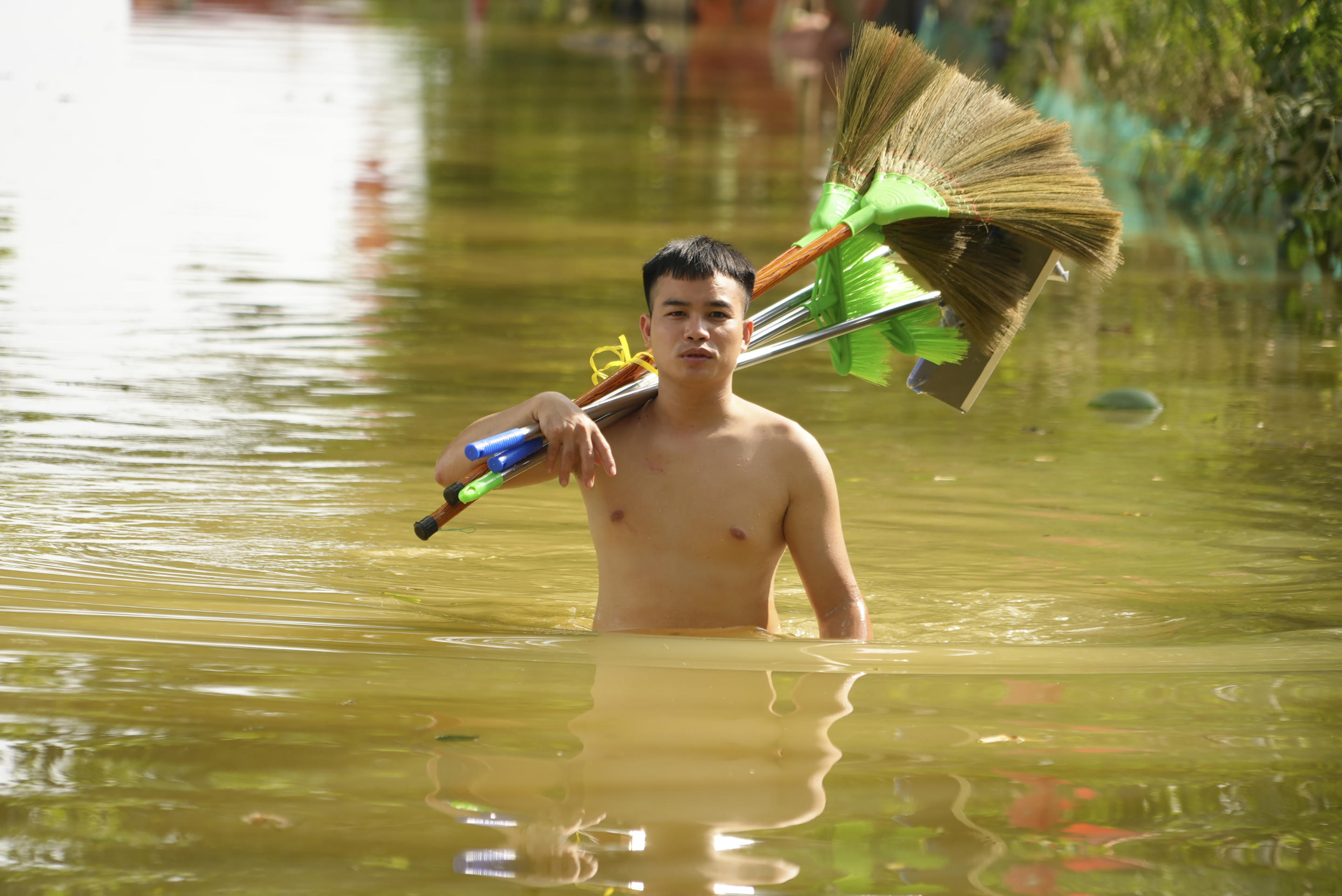 A man wades in flood carrying brooms to clean up houses as flood starts to recede in the aftermath of Typhoon Yagi in An Lac village, Hanoi, Vietnam Friday, Sept. 13, 2024. (Hau Dinh/AP)