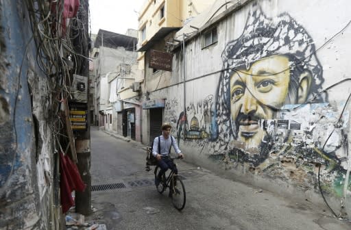 Mohammed rides his bicycle past a mural painting of the late Palestinian leader Yasser Arafat south of the Lebanese capital Beirut on May 29, 2018