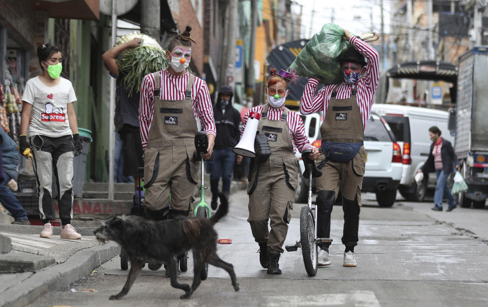 Los miembros del grupo "Circo Encuentro" caminan por una calle con alimentos donados que recibieron a cambio de sus presentaciones en Bogotá, Colombia, el sábado 4 de julio de 2020. El grupo de artistas callejeros creado hace más de una década se dedica ahora a intercambiar su show por alimentos para ayudar a personas en los barrios más pobres al sur de la capital colombiana impactados por la pandemia del nuevo coronavirus. (Foto AP/Fernando Vergara)