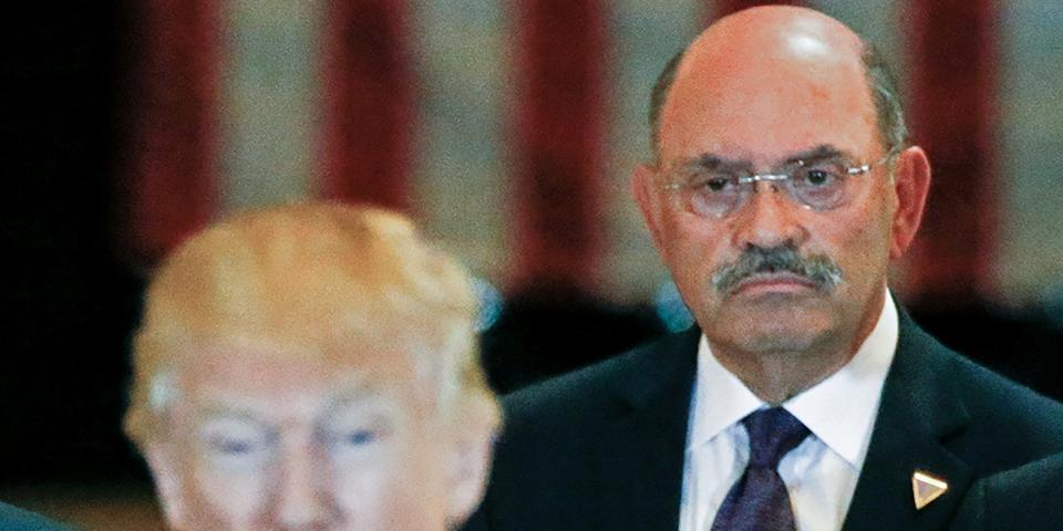 Allen Weisselberg in focus behind Donald Trump, with a US flag visible in the background.