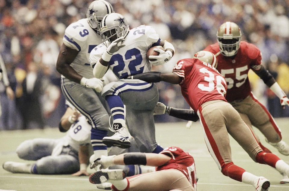 FILE - Dallas Cowboys running back Emmitt Smith (22) makes his way through San Francisco 49ers' defensive backs Merton Hanks (36) and Bill Romanowski (53), for a 4-yard gain in the second quarter of the Cowboy's 38-21 NFC championship win, Sunday, Jan. 23, 1994, in Irving, Texas. The 49ers-Cowboys playoff history is a rich one from back-to-back conference title games in the early 1970s, the iconic “Catch” in the 1981 season and then the heated rivalry in the 1990s when the Cowboys won the first two meetings on the way to Super Bowl titles and then the Niners took the third game. (AP Photo/Eric Gay, File)