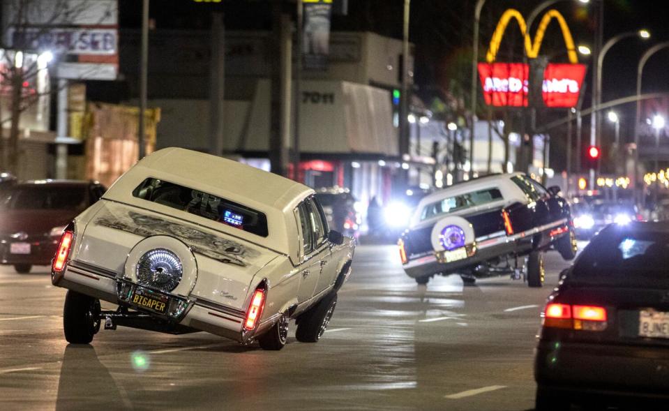 Hydraulics cause lowriders to bounce from side to side on a city street at night.