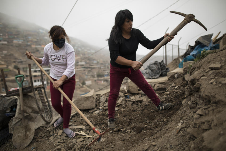 En esta foto del 12 de junio de 2020, Clara Arango y su hija Kimberly aflojan el suelo para colocar un piso de cemento mientras trabajan para expandir su hogar, en el barrio Nueva Esperanza de Lima, Perú. Madre soltera de dos hijos, perdió su trabajo cuando su empleador cerró su centro comercial en el barrio más rico de Lima debido a la cuarentena para frenar la propagación del nuevo coronavirus que comenzó el 16 de marzo. (AP Foto/Rodrigo Abd)