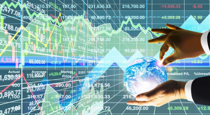 A concept image showing hands holding a globe with stock charts in the background.