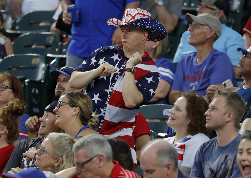 FILE - In this July 4, 2019, file photo, a fan dressed for the Fourth of July holiday dances to music in the stadium in the fifth inning of a baseball game between the Los Angeles Angels and the Texas Rangers in Arlington, Texas. Major League Baseball owners gave the go-ahead Monday, May 11, 2020, to making a proposal to the players’ union that could lead to the coronavirus-delayed season starting around the Fourth of July weekend in ballparks without fans, a plan that envisioned expanding the designated hitter to the National League for 2020. (AP Photo/Tony Gutierrez, File)