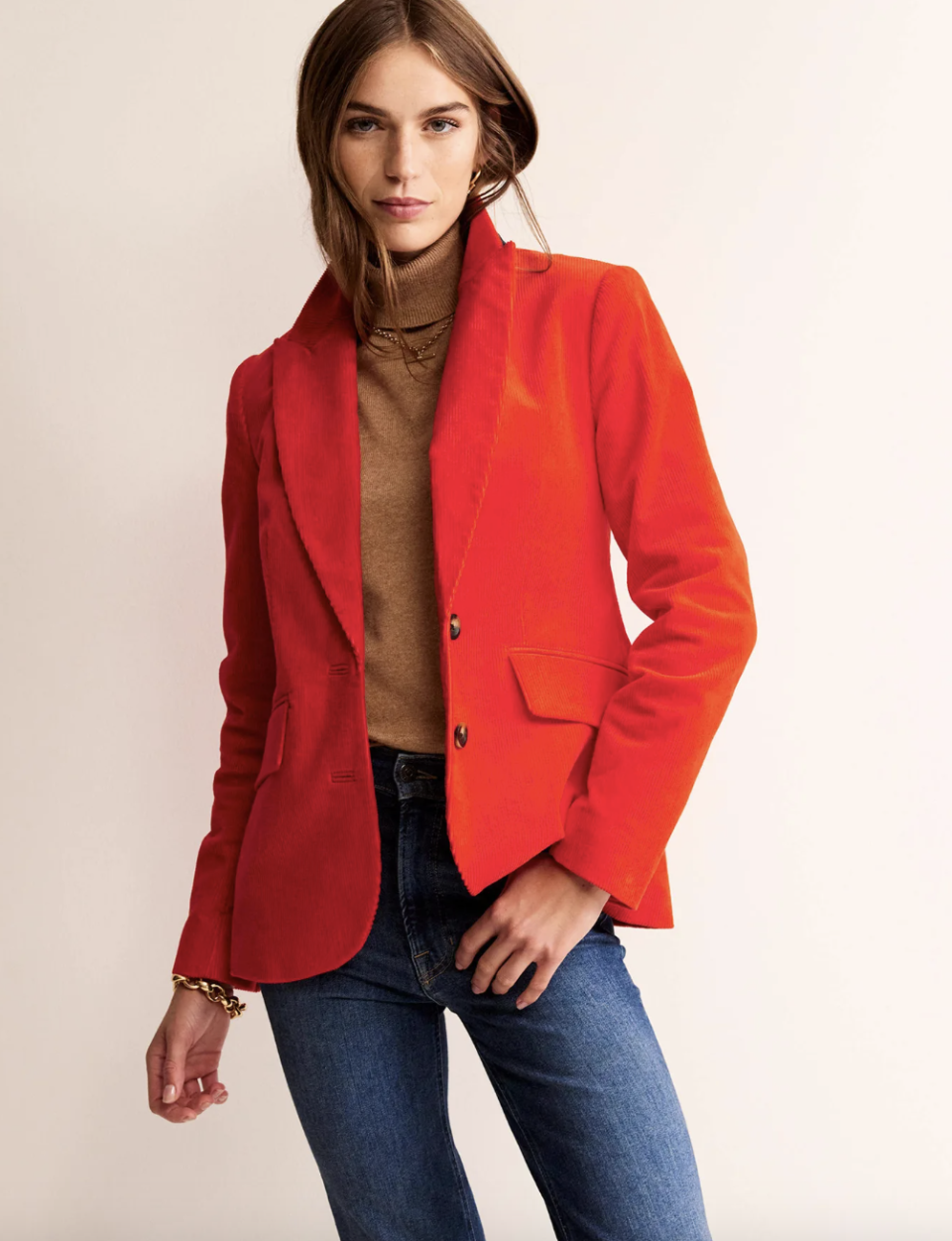 model wearing blue jeans, brown turtleneck and bright red Marylebone Cord Blazer in Admiral (Photo via Boden)