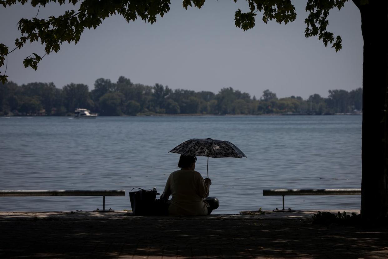 A person stays cool under an umbrella near the Lake Ontario shoreline in Toronto. (Evan Mitsui/CBC - image credit)