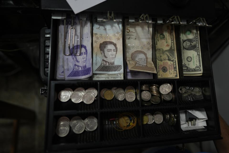 A cash register drawer holds Bolivars and U.S. currencies at a shop in Caracas, Venezuela, Friday, May 13, 2022. A new tax law approved by the Venezuelan government, that went into effect in March, applies a 3% tax charge on transactions paid in foreign currencies. (AP Photo/Ariana Cubillos)