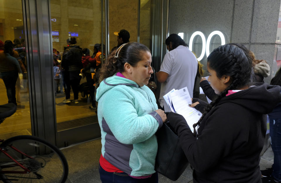 Two women look over their documents by a line snaking around the block outside a U.S. immigration office with numerous courtrooms Thursday, Jan. 31, 2019, in San Francisco. The crowd was mixed with people who had court appointments for Thursday, people whose appointments were swallowed up by shutdown and others who had 'Notices to Appear' but assumed that meant they had court dates. (AP Photo/Eric Risberg)