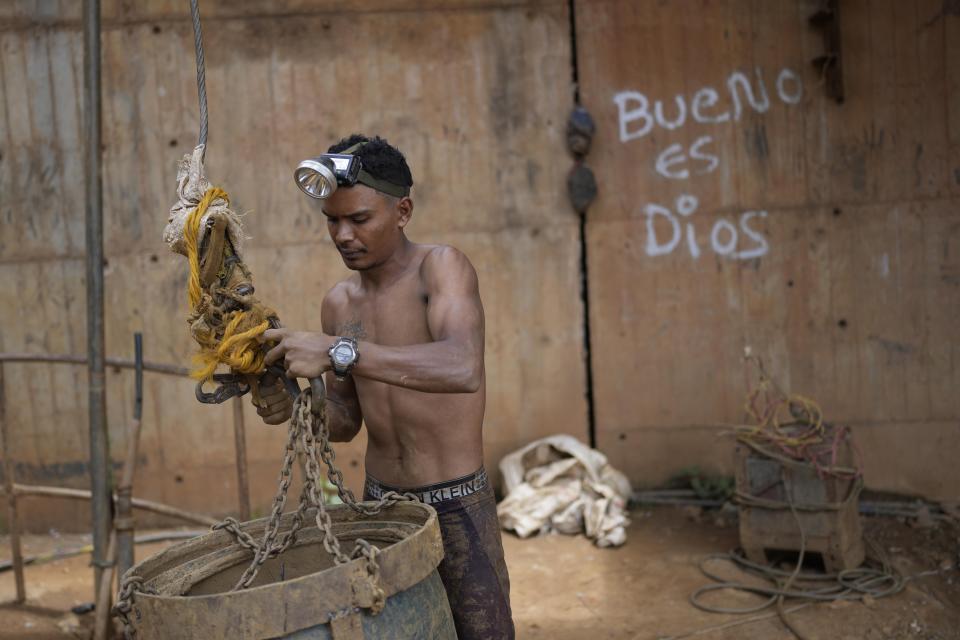 Un trabajador sujeta un gran cubo a un sistema de poleas para subir piedras por un pozo en una mina subterránea de oro en El Callao, estado Bolívar, en Venezuela, el viernes 28 de abril de 2023. Los cubos también son utilizados para subir y bajar herramientas en el lugar. (AP Foto/Matias Delacroix)