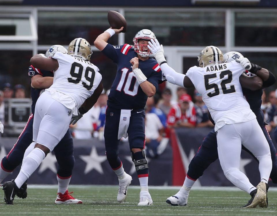 Patriots quarterback Mac Jones releases a pass under pressure from Saints defenders.