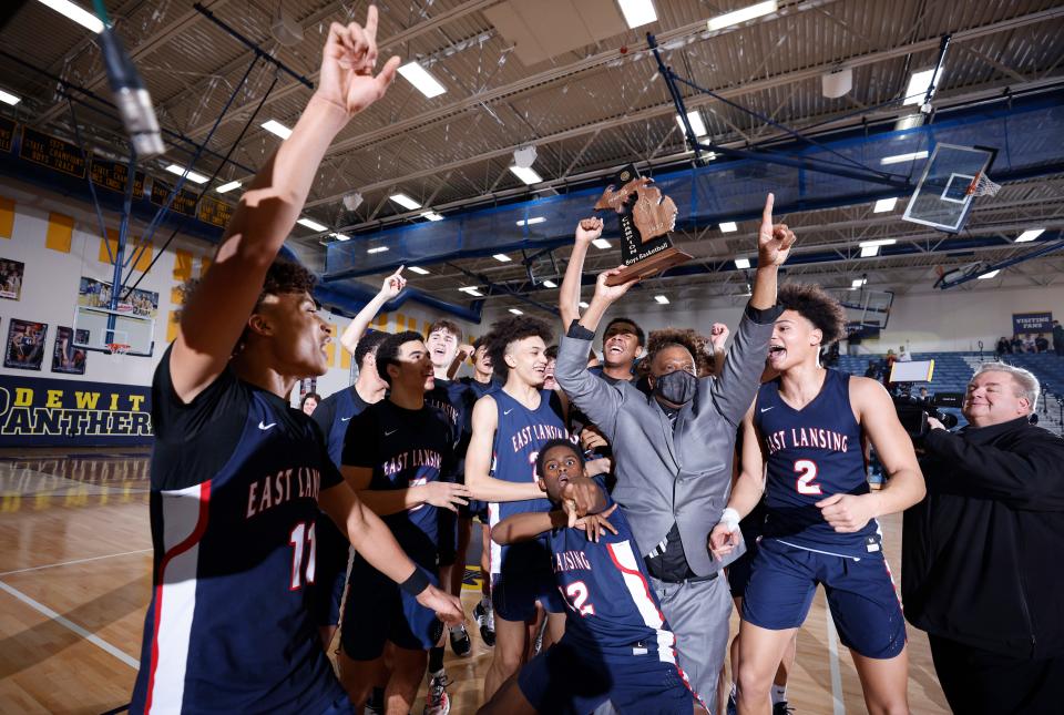 East Lansing players and coach Ray Mitchell celebrate with their district championship trophy after defeating Grand Ledge, Friday, March 11, 2022, at DeWitt High School. East Lansing won 57-44.