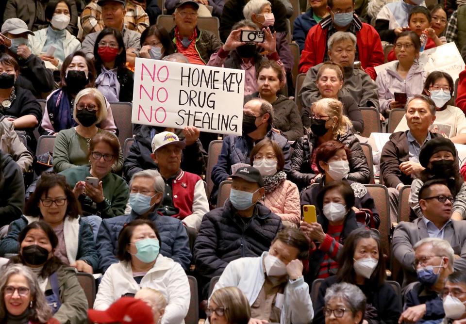 Rows of people are seated, with one holding a sign that says, "No Home Key, no drug, no stealing."