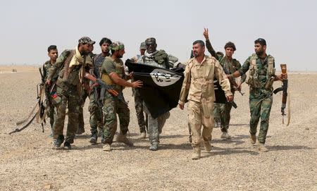 Iraq's Shi'ite paramilitaries and members of Iraqi security forces hold an Islamist State flag which they pulled down in Nibai, in Anbar province May 26, 2015. REUTERS/Stringer