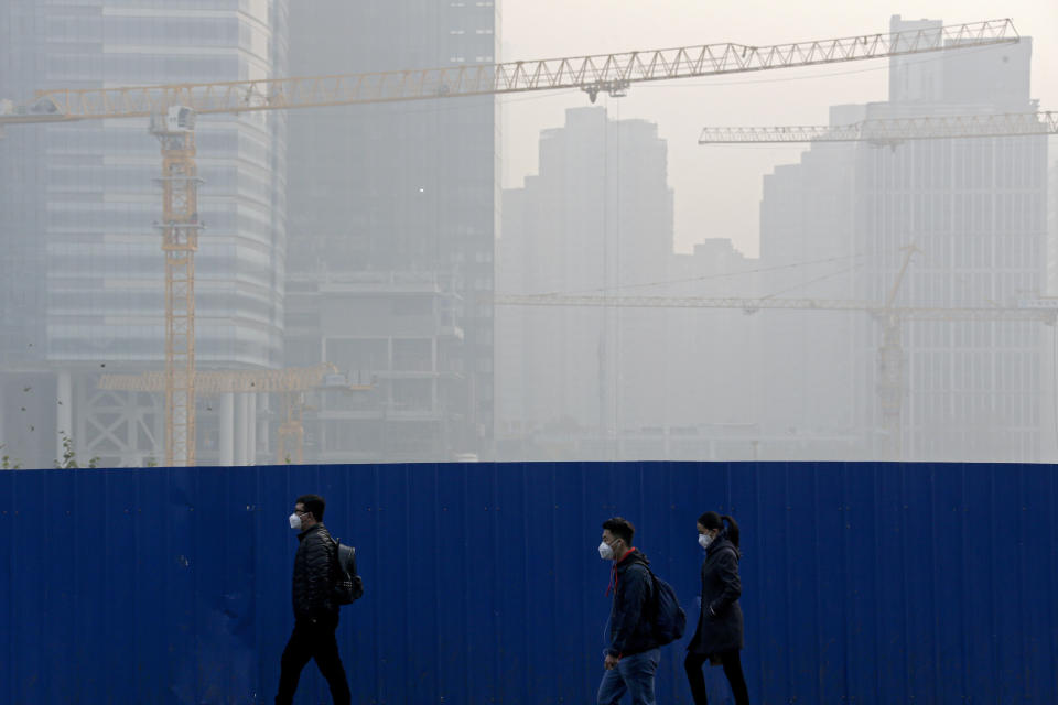 People wear masks for protection against the pollution as they walk by a construction site at the Central Business District chocked with haze in Beijing, Tuesday, Nov. 13, 2018. The potential damage to global trade brought on by President Donald Trump's tariffs battle with Beijing is looming as leaders of Southeast Asian nations, China, the U.S. and other regional economies meet in Singapore this week. (AP Photo/Andy Wong)