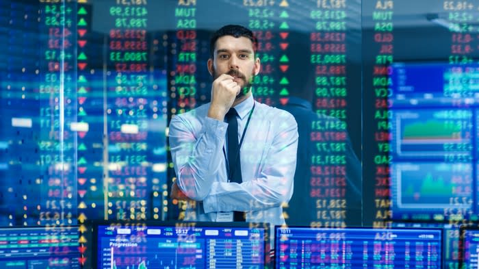 A man in a shirt and tie watches stock ticker numbers and graphs.