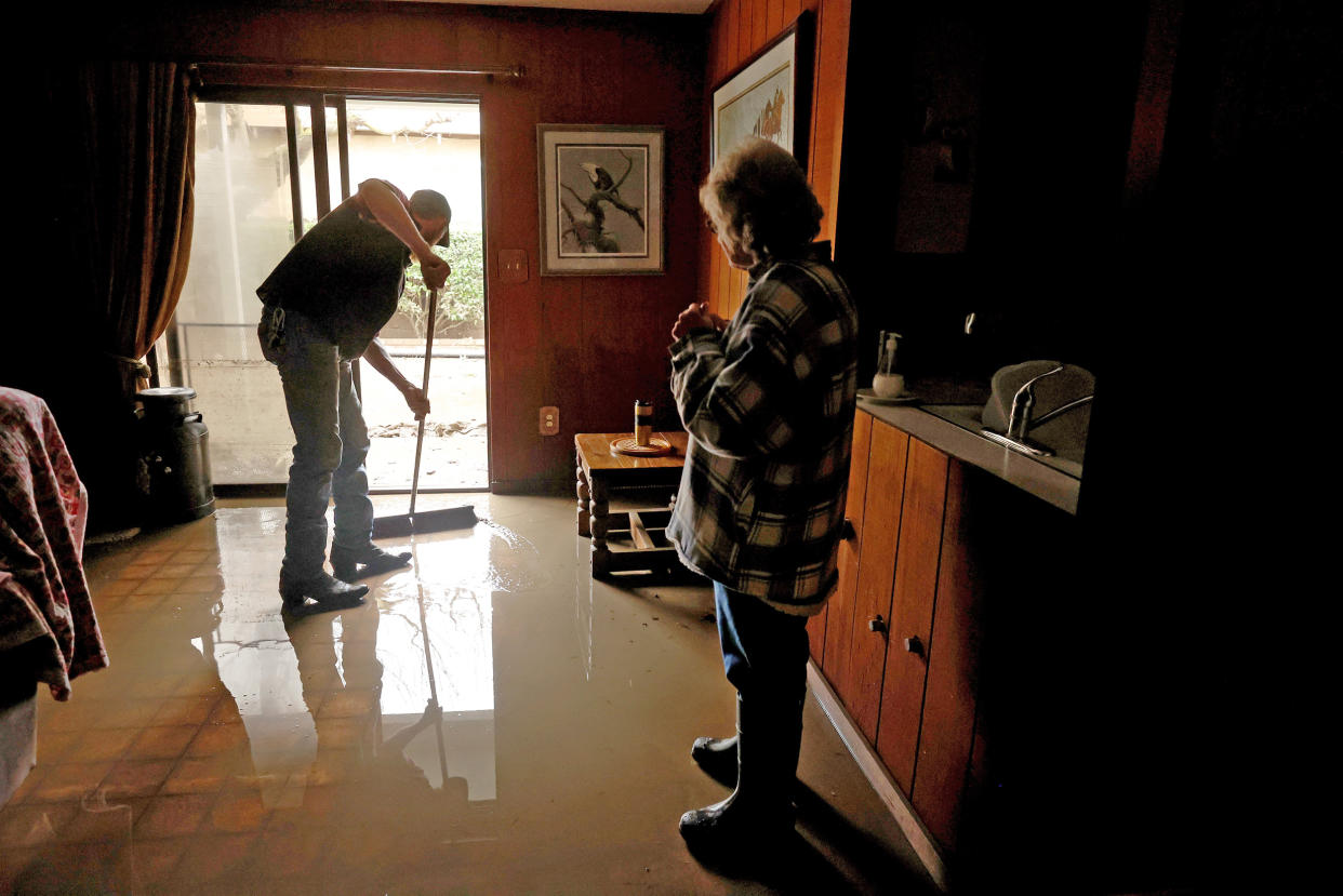 Lana Spurlock, right, looks on as Dakota Boone sweeps water out of her flooded home on Jan. 11, 2023 in Planada, Calif. (Justin Sullivan / Getty Images)