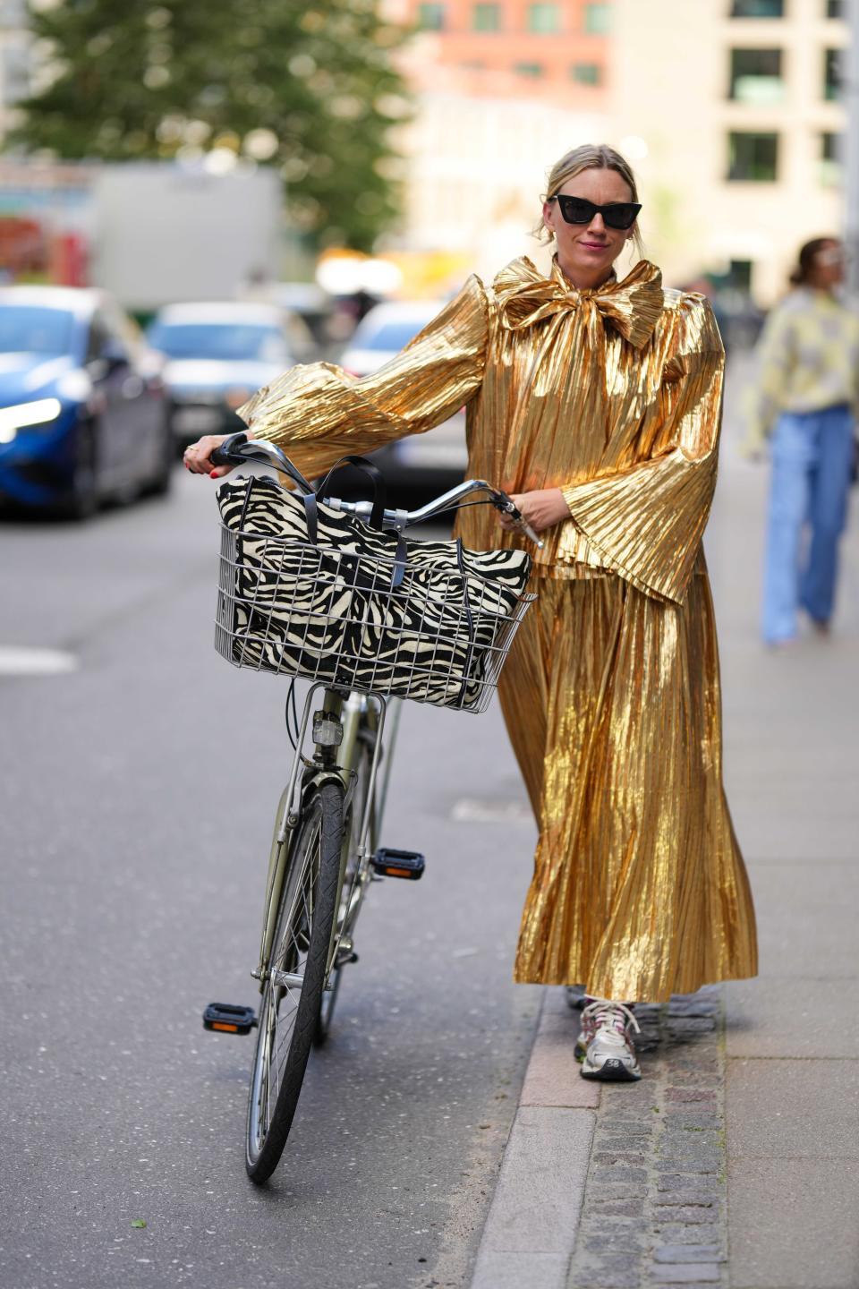 A guest with a bicycle wearing a gold dress and sneakers at Copenhagen Fashion Week