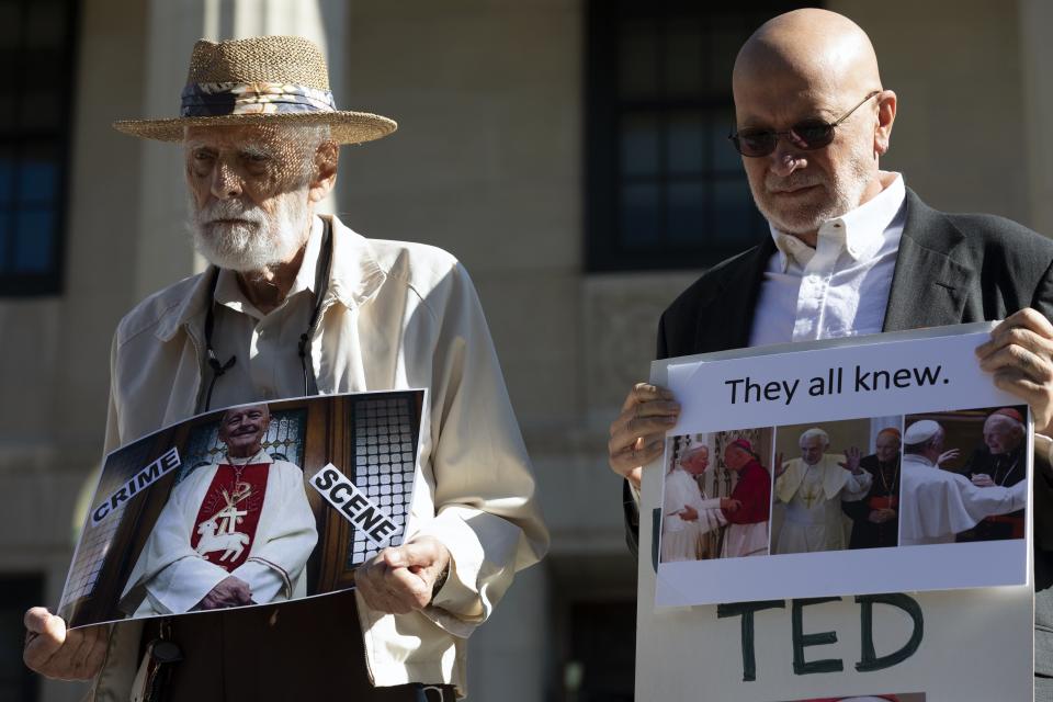 Stephen Sheehan, left, and Skip Shea hold signs during a news conference outside Dedham District Court following the arraignment of former Cardinal Theodore McCarrick, Friday, Sept. 3, 2021, in Dedham, Mass. McCarrick has pleaded not guilty to sexually assaulting a 16-year-old boy during a wedding reception in Massachusetts nearly 50 years ago. (AP Photo/Michael Dwyer)