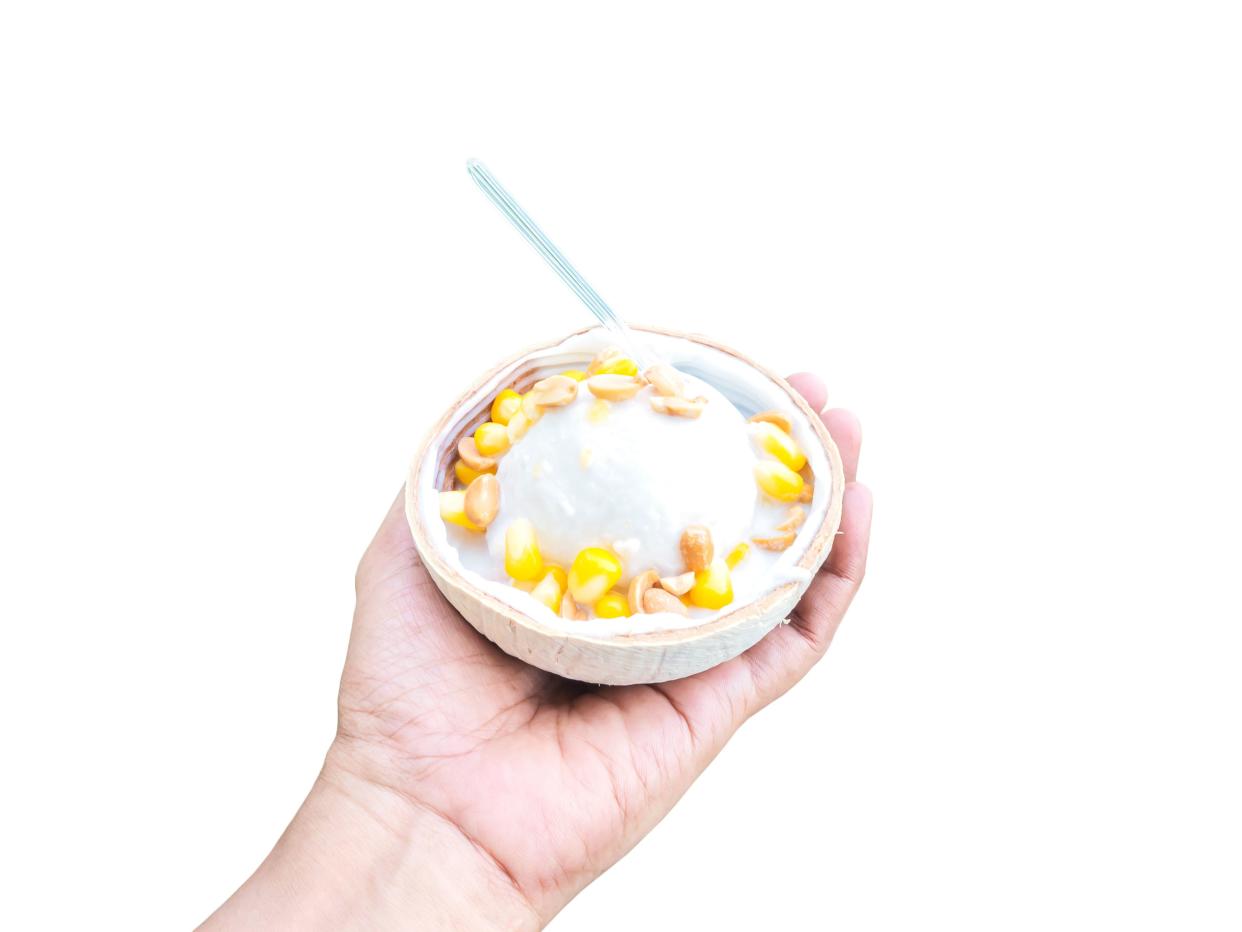 Close up hand holding coconut ice cream with topping, isolated