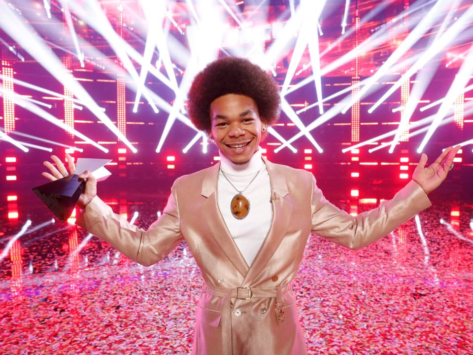 Cam Anthony holding his winning trophy in front of a red, strobe-light background on "The Voice"