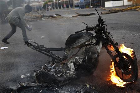 An anti-government demonstrator walks behind a burning motorcycle during a protest in San Cristobal, about 410 miles (660 km) southwest of Caracas, February 27, 2014. REUTERS/Carlos Garcia Rawlins