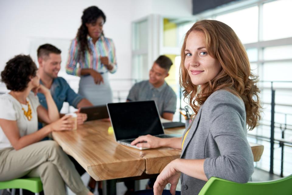 A conference room bustling with conversation, one participant smiles at the camera.