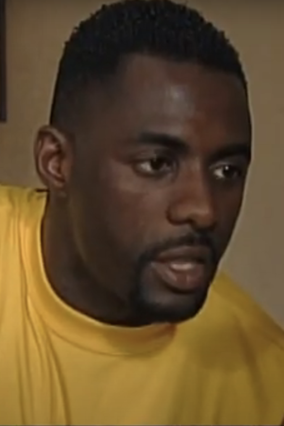 Idris Elba in a yellow shirt looking intently at something off-screen in a scene from a film or TV show