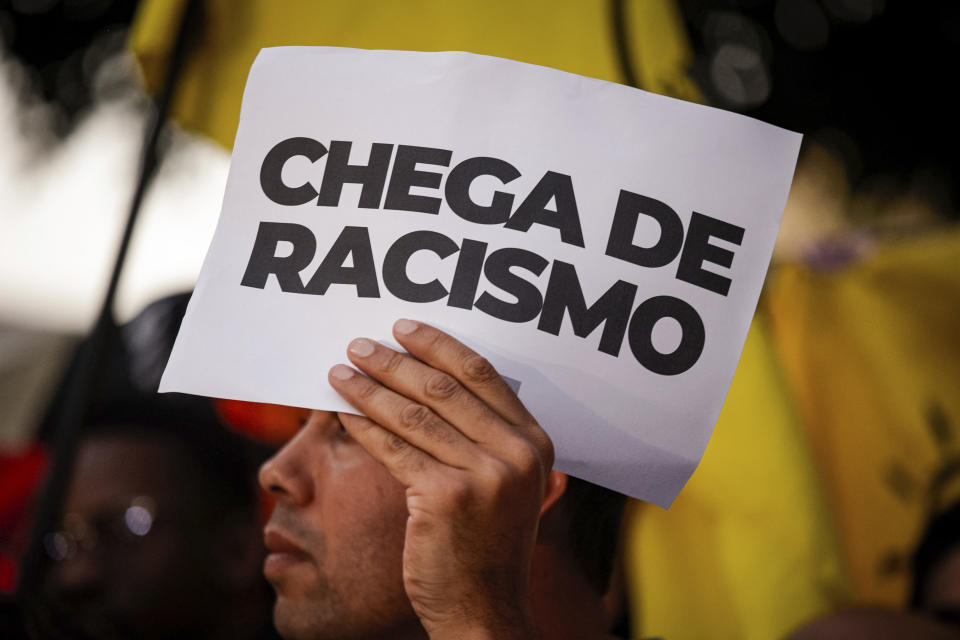 A man holds a sign with a message that reads in Portuguese; "Enough of racism", during a protest against the racism suffered by Brazilian soccer star Vinicius Junior who plays for Spain's Real Madrid, outside the Spanish Consulate in Sao Paulo, Brazil, Tuesday, May 23, 2023. Vinicius, who is Black, has been subjected to repeated racist taunts since he arrived in Spain five years ago. (AP Photo/Tuane Fernandes)