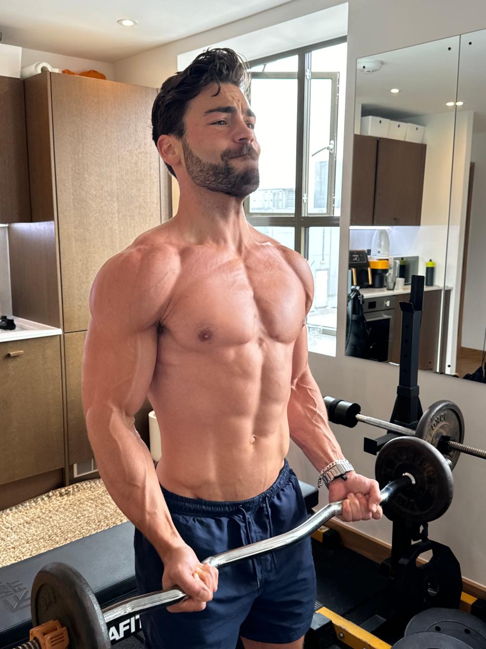 A man in a small gym performing a barbell exercise