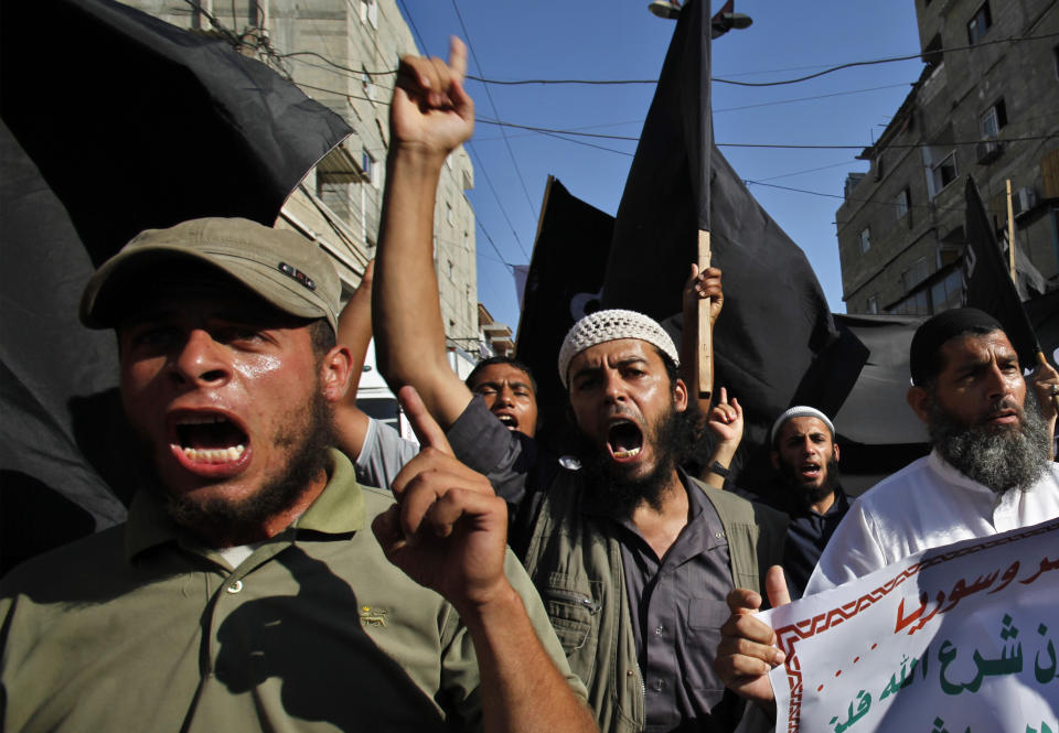 FILE - In this Thursday, Aug. 22, 2013 file photo, Palestinian members from Youth Salafists group chant slogans while waving their black flags during a protest against the Egyptian and Syria regimes in Rafah Refugee Camp, southern Gaza Strip. Arabic on poster reads "Criminals and murderers". A leader of one of Gaza’s secretive salafist militant groups says the al-Qaida-inspired movement now has several thousand armed fighters in the seaside strip, posing a formidable threat to both Israel and the area’s Hamas rulers. (AP Photo/Adel Hana, File)