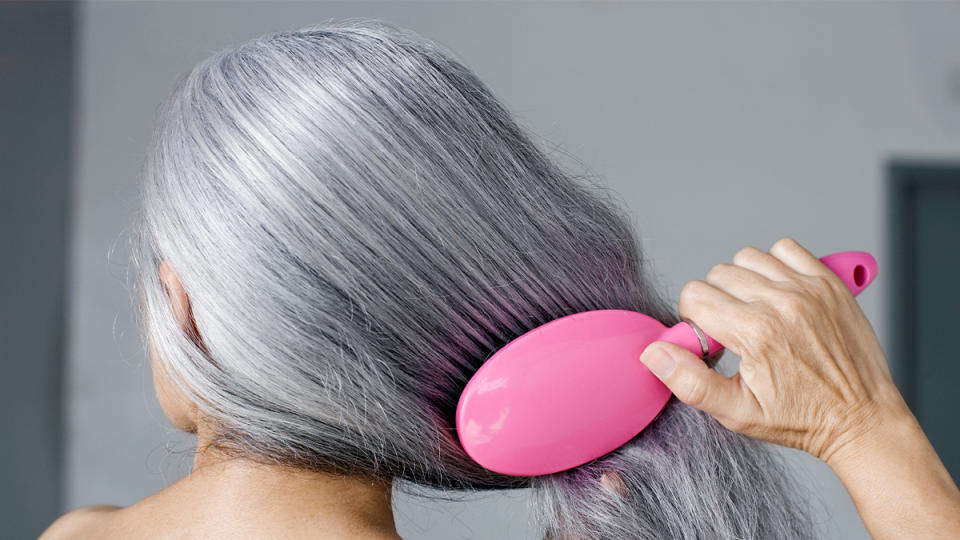 gray haired woman brushing her hair in the back 