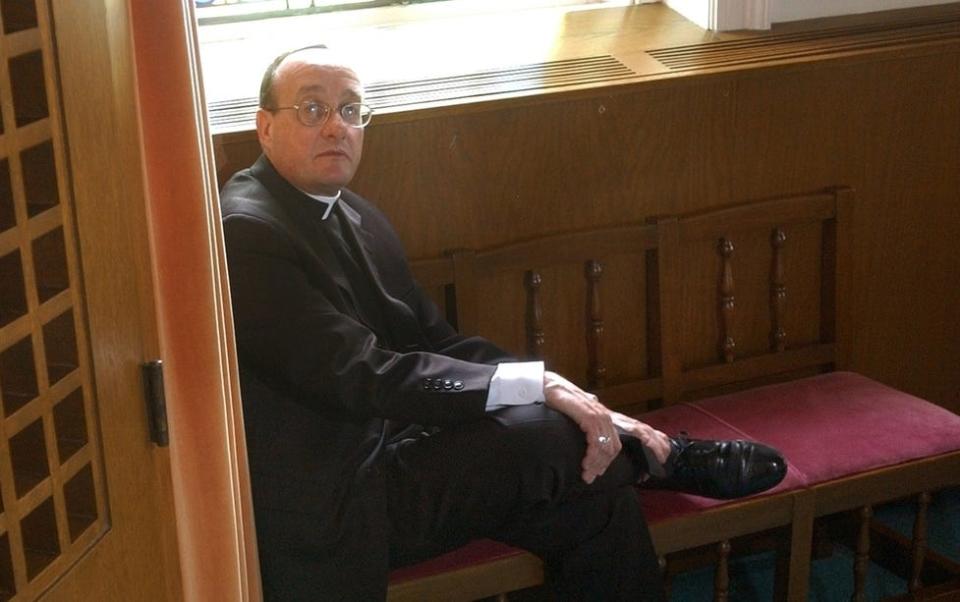 A 2002 photo shows the Rev. Kevin Fisette outside the confessional at Our Lady Chapel at Holy Name Church in Providence.