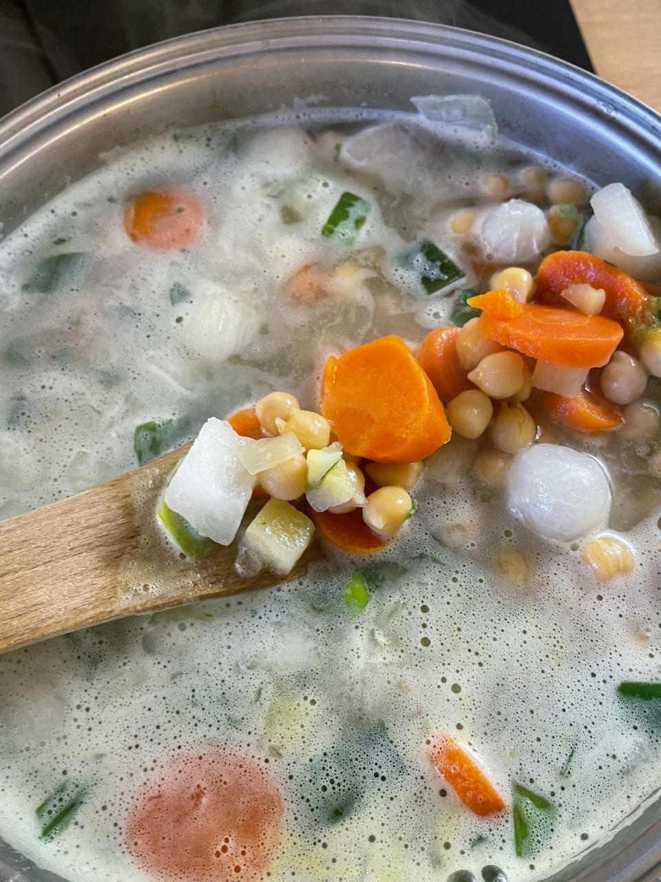 Diced vegetables and chickpeas simmering with water in saucepan.