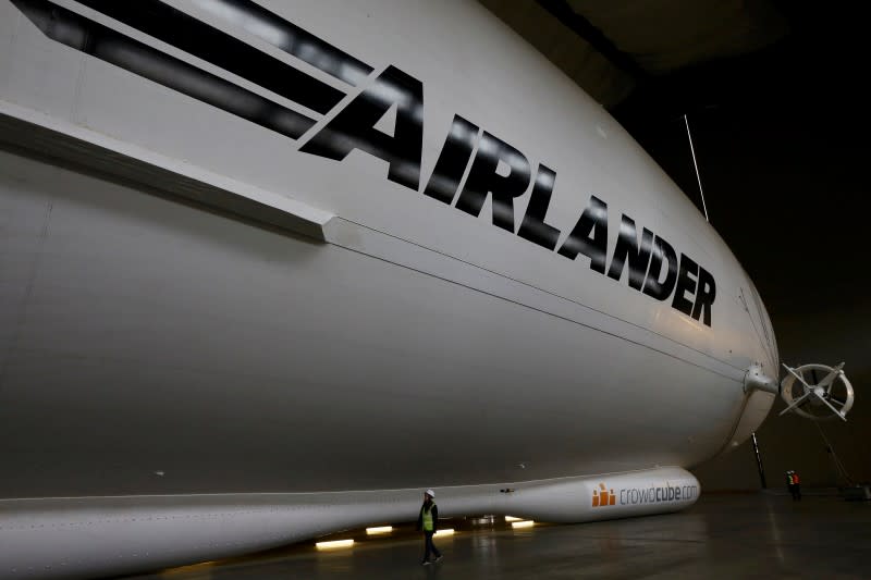 A worker walks alongside the Airlander 10 hybrid airship during its unveiling in Cardington, Britain March 21, 2016. The Airlander can take off and land vertically meaning it does not need a tarmac runway. It can also operate from open fields, deserts, ice or water, meaning it could be useful for humanitarian missions or coastguard monitoring. REUTERS/Darren Staples