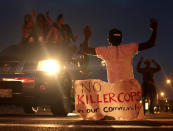 <p>People protest Sunday, Aug. 17, 2014, for Michael Brown, who was killed by a police officer last Saturday in Ferguson, Mo. As night fell Sunday in Ferguson, another peaceful protest quickly deteriorated after marchers pushed toward one end of a street. Police attempted to push them back by firing tear gas and shouting over a bullhorn that the protest was no longer peaceful. (AP Photo/Charlie Riedel) </p>