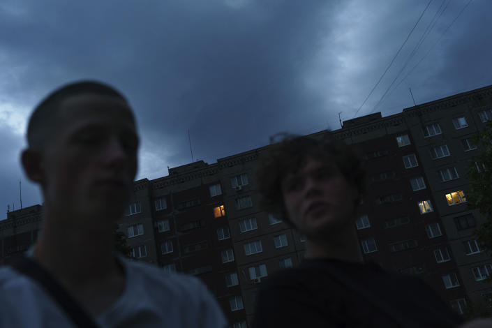 The lights in just a few windows illuminate an otherwise dark apartment block as Roman Kovalenko, 19, left, visits his friend, Oleksandr Pruzhyna, 18, right, in Kramatorsk, Donetsk region, eastern Ukraine, Friday, Aug. 12, 2022. "It's a completely different feeling when you go outside. There is almost no one on the streets, I have the feeling of being in an apocalypse," said Pruzhyna, who lost his job at a barber shop after the invasion, and now spends most of his time at home playing computer games. "I feel like everything I was going to do became impossible, everything collapsed in an instant." (AP Photo/David Goldman)