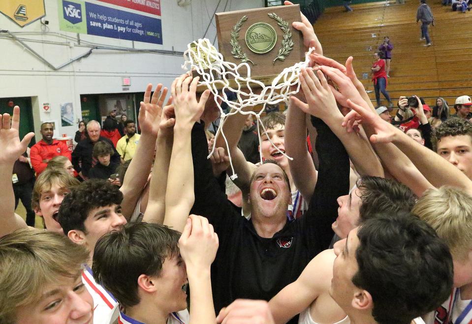 CVU coach Mike Osborne hoists the championship trophy after his Redhawks defeated Rice 42-38 to claim the schools first D1 title basketball title on Saturday night.