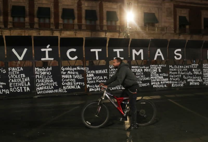 A man rides a bicycle past the names of victims of femicide in Mexico painted by women on fences placed outside the National Palace ahead of a Women's Day protest, in Mexico City