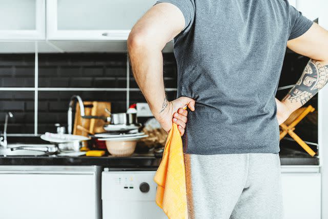 <p>da-kuk/Getty</p> man standing with hands on hips in kitchen