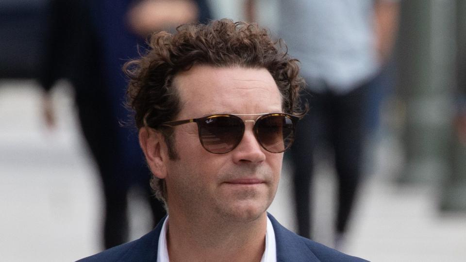 actor danny masterson holding a coffee and wearing sunglasses as he walks down the street toward a courthouse