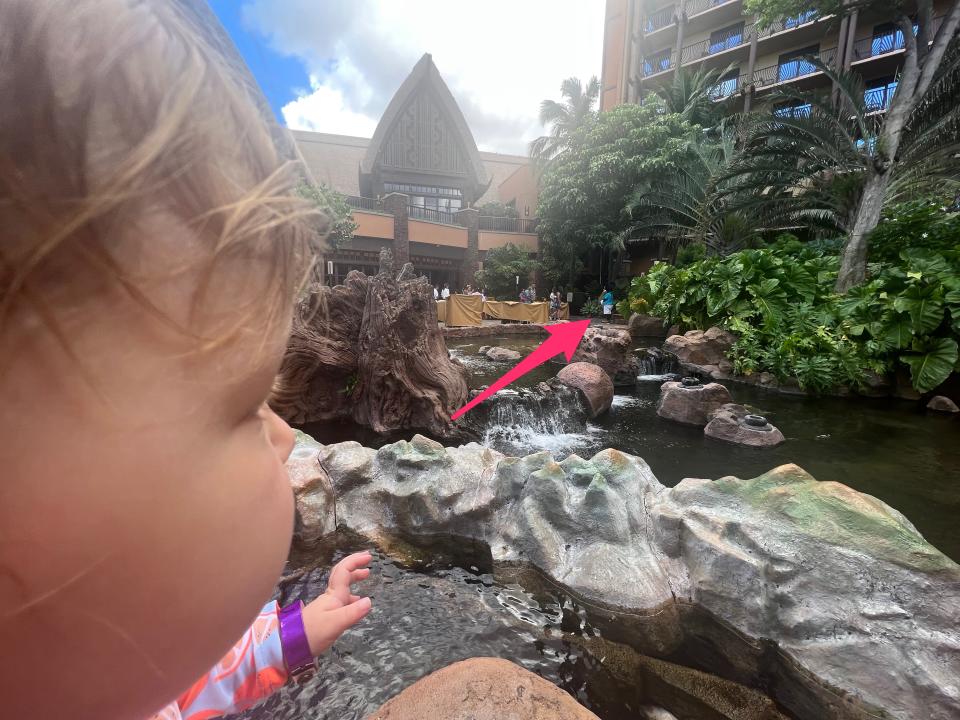 A close up of the side of a baby's face looking at Mickey Mouse in the distance with an arrow pointing to Mickey.