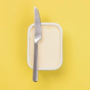 tub of margarine with a knife resting on top on a yellow background