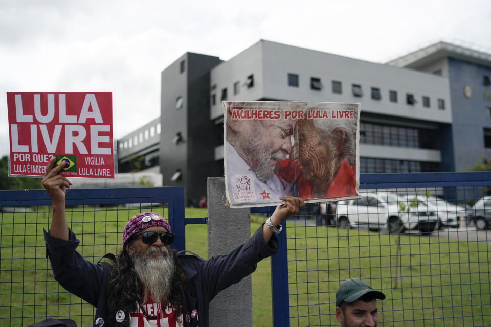 A supporter of Brazil's former President Luiz Inacio Lula da Silva holds up signs that reads in Portuguese "Free Lula," left, and "Women for Lula free." outside the Federal Police headquarters where the former leader is imprisoned in Curitiba, Brazil, Friday, Nov. 8, 2019. Da Silva's lawyers have begun legal procedures requesting his release from prison, following a Supreme Court decision late Thursday that a person can be imprisoned only after all appeals to higher courts have been exhausted. Da Silva has been detained since April 2018 after being convicted of corruption. (AP Photo/Leo Correa)