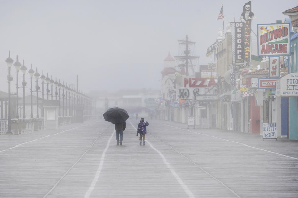 A man shields himself from the rain with an umbrella as he walks along with a child during a rainy and foggy winter afternoon at the Ocean City boardwalk in Ocean City, N.J. (Jose F. Moreno/The Philadelphia Inquirer via AP)