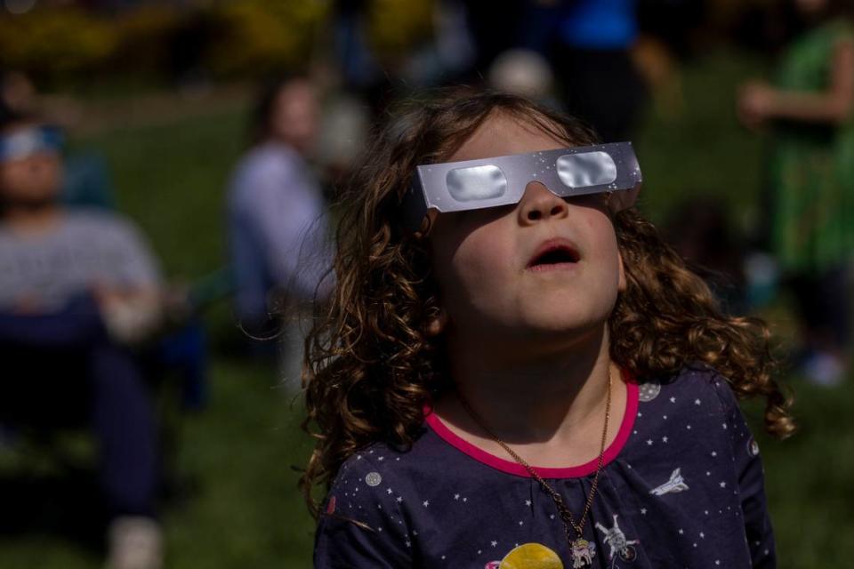 Six-year-old Evey Churchill wears protective glasses while viewing the solar eclipse during a watch party at the Morehead Planetarium and Science Center at UNC-Chapel Hill on Monday, April 8, 2024.