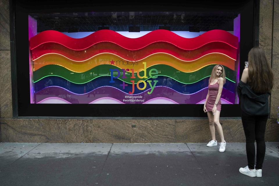 In this Wednesday, June 19, 2019, photo, a visitor to Herald Square takes a photo with the Pride and Joy window display at the Macy's flagship store in New York. For Pride month, retailers across the country are selling goods and services celebrating LGBTQ culture. Macy’s flagship store is adorned with rainbow-colored Pride tribute windows, set in the same space as its famous Christmas displays. (AP Photo/Mary Altaffer)